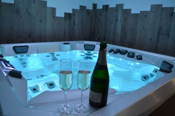 A hot tub with two champagne glasses and a bottle, surrounded by wooden panels.