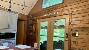 L’intérieur chaleureux d’un chalet comprend un coin repas, des murs en bois, un ventilateur de plafond et une grande fenêtre donnant sur un paysage verdoyant.