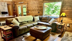Un intérieur de chalet chaleureux avec un canapé en cuir, un petit pouf, une table basse en bois et un tapis en peau de vache.