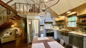 Une cuisine moderne avec un coin repas, des appareils électroménagers en acier inoxydable et un escalier menant à un niveau supérieur.