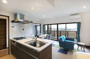 Een moderne keuken met een ingebouwde kookplaat, spoelbak en afzuigkap. Er is een eethoek met een tafel en stoelen, en een balkon met uitzicht op de stad.