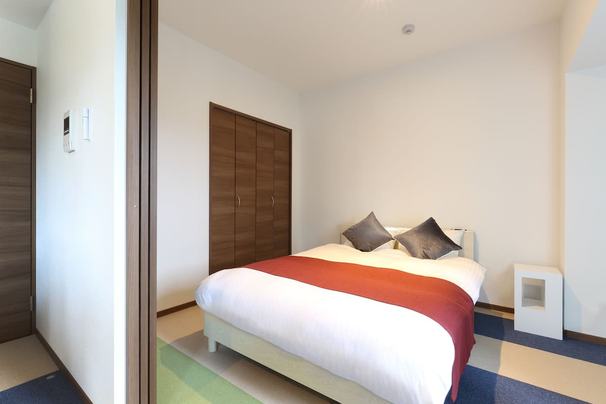 A hotel room with a bed, a wardrobe, and a bedside table.