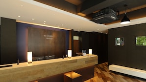 A reception area with a wooden reception desk, two illuminated lamps, a large wall-mounted sign, and a ceiling-mounted projector. - Grand Residence Hakataeki Minami (Fukuoka)