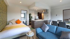 A modern hotel room with a bed, a blue sofa, a small round table, a kitchenette, and a dining area. - Grand Residence Hakataeki Minami (Fukuoka)