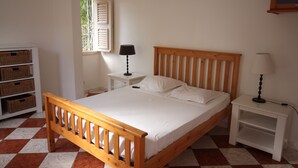A bedroom with a wooden bed, white bedding, a nightstand with a lamp, and a window with shutters. - Confortable Villa "Coco" with a private swimming pool (Saint François)