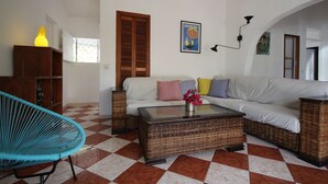 A living room with a checkered floor, a sofa with colorful cushions, a wicker coffee table, a blue chair, and a wooden cabinet. - Confortable Villa "Coco" with a private swimming pool (Saint François)