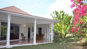 A house with a covered porch, a dining area with chairs, and a garden with large plants and flowers. - Confortable Villa "Coco" with a private swimming pool (Saint François)