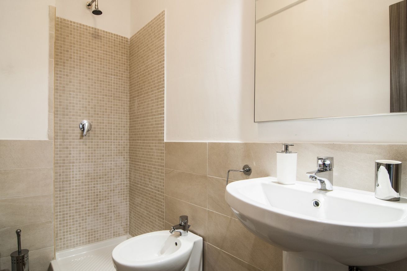 A bathroom with a shower, a bidet, a sink, and a mirror.