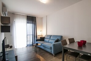 Un salon moderne avec un canapé, une table à manger et des chaises, un téléviseur et une fenêtre avec des rideaux.