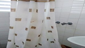 Un bany amb una paret revestida de rajoles blanques, un lavabo blanc i una cortina de dutxa amb dibuixos geomètrics.