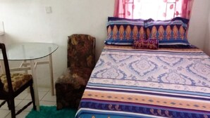 Una habitació petita amb una taula de vidre, un estriatge de llit estampat i una catifa verda.