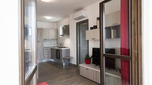 Een moderne keuken met een fornuis, spoelbak en kastjes, een klein zithoekje met een tafel en stoelen, en een schuifpui naar een balkon.