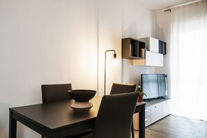Un espace de repas moderne comprenant une table, des chaises, un bol, une lampe et un téléviseur posé sur un meuble.