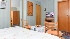 Een hotelkamer met een bed, twee houten stoelen, een kleine tafel met fruit, een televisie en een kledingkast.