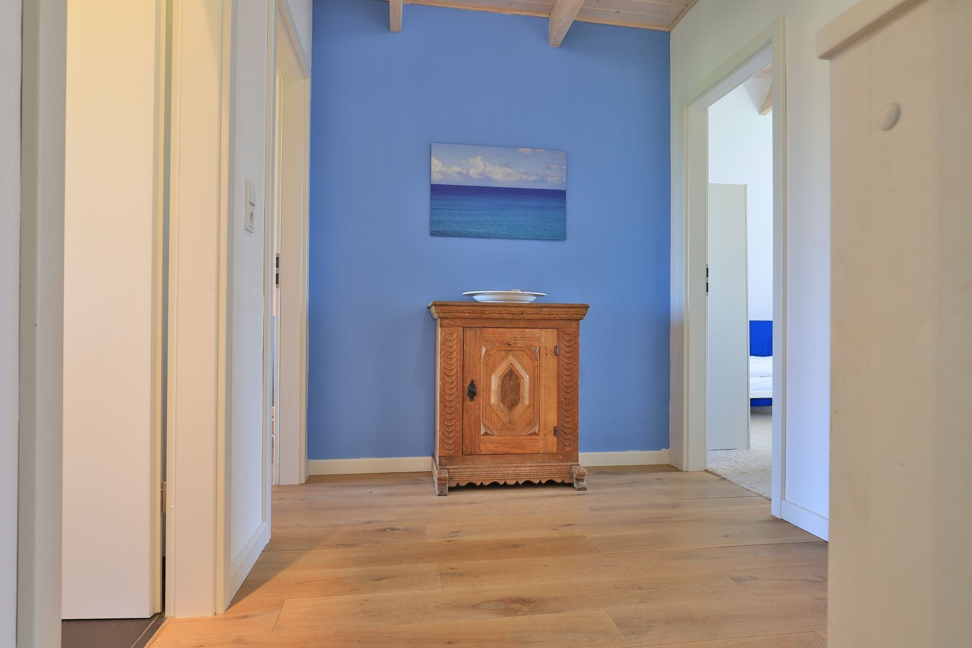 Een hal met houten vloer, een blauwe muur en een houten kastje met een kom erop.