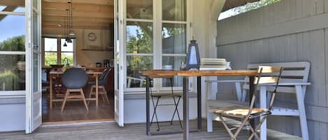 An open patio with a wooden table and chairs, a lantern, and a view of the interior kitchen and dining area.