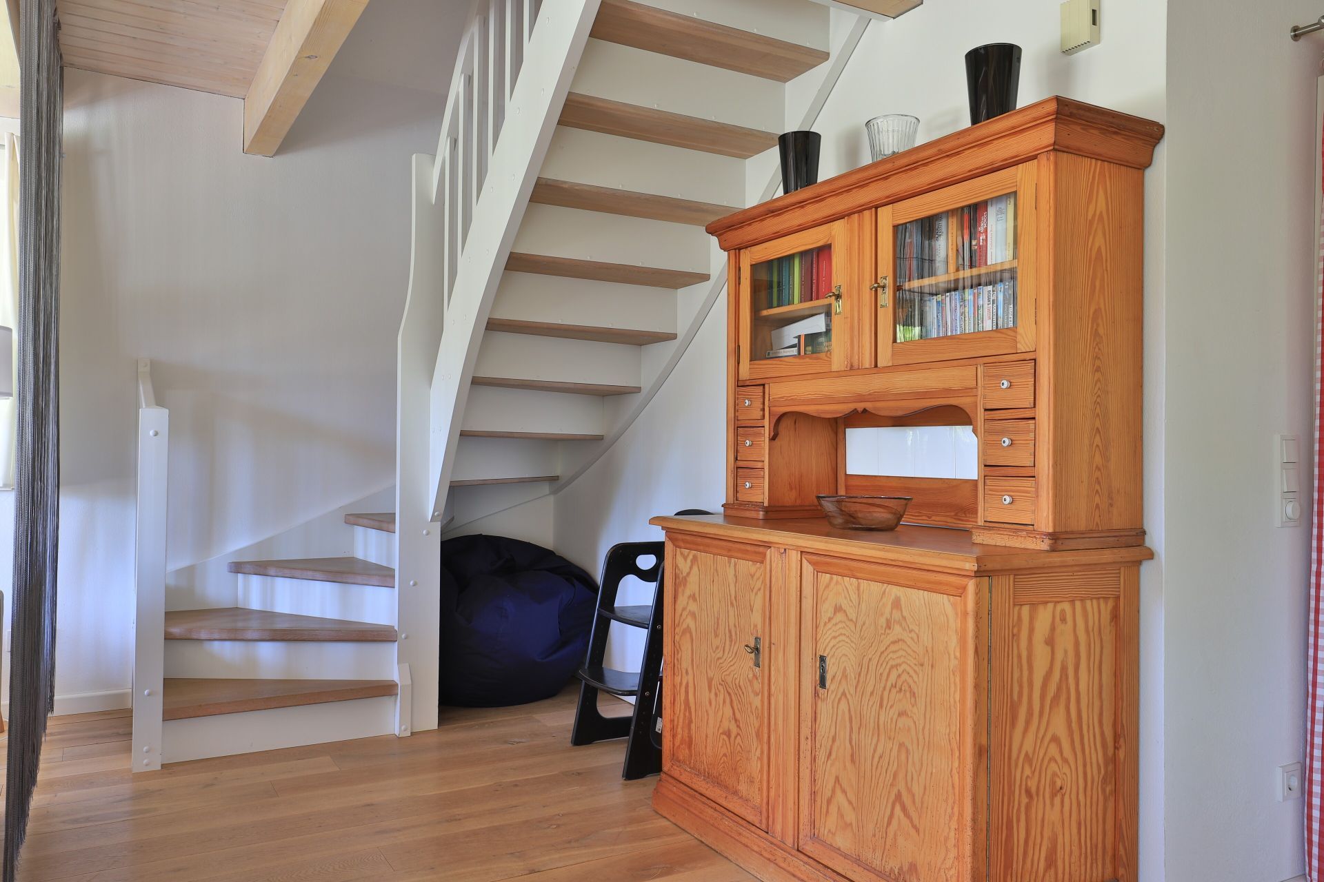 Un escalier avec des marches en bois et un meuble en bois doté de portes en verre, dans lequel sont rangés des livres.