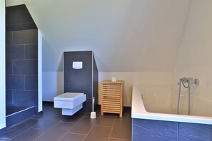 A modern bathroom with a built-in toilet, a wooden stool, and a freestanding bathtub.