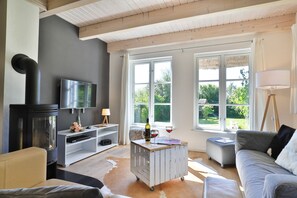 A living room with a TV, a fireplace, a sofa, and large windows.