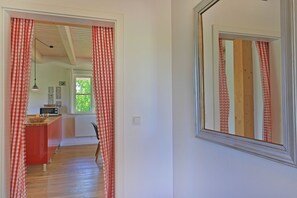 A hallway with a red and white checkered curtain, a wooden floor, a microwave, and a small kitchen area with a red cabinet.