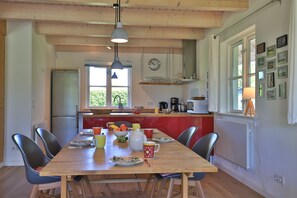 Uma área de refeições com uma mesa de madeira, cadeiras e uma cozinha ao fundo.