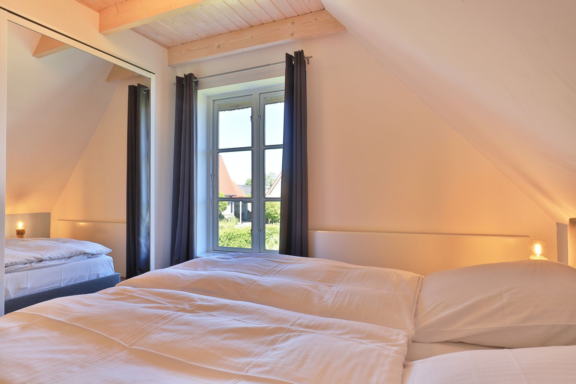 A bedroom with two beds, a large window with curtains, and a sloped ceiling.