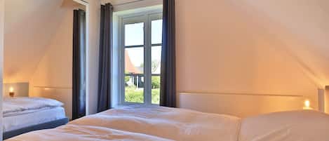 A bedroom with two beds, a large window with curtains, and a sloped ceiling.
