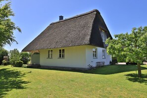 A house with a thatched roof, a small porch, and a well-maintained lawn.