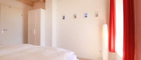 Un dormitorio con cama, armario y una pared decorada con cuadros.