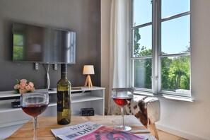 Uma sala de estar moderna com uma janela ampla, uma televisão de tela plana, uma garrafa de vinho e duas taças de vinho sobre uma mesa de madeira.