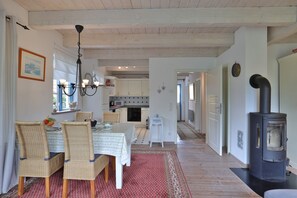 A dining area with wicker chairs, a table with a tablecloth, a chandelier, and a kitchen in the background.