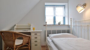A bedroom with a bed, a desk, a chair, a window with curtains, and a wall-mounted lamp.