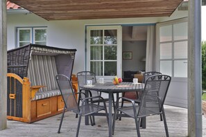Un patio couvert avec une table et des chaises, un canapé en osier et une vue sur l’intérieur de la maison.