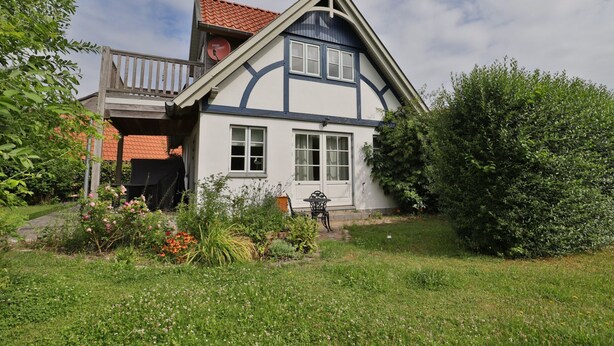 A two-story house with a balcony, a satellite dish, and a garden with various plants and flowers.