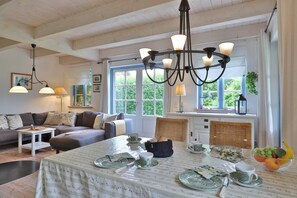 Una sala de estar acogedora con comedor, vigas de madera en el techo y un ventanal con vistas a zonas verdes.