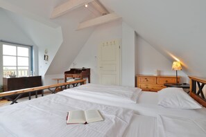 A bedroom with a large bed, a desk, a dresser, and a window.