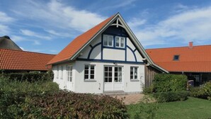 Een tweelaags huis met een rode dakbedekking, witte muren en een voordeur.