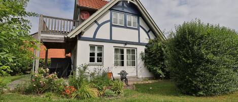 Una casa de dos pisos con balcón, antena parabólica y jardín con diversas plantas y flores.