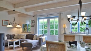 A cozy living room with a sofa, a dining table with chairs, and a large window with a view of greenery.