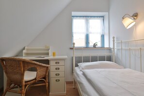 Une chambre à coucher comprenant un lit, un bureau, une chaise, une fenêtre avec des rideaux et une lampe fixée au mur.