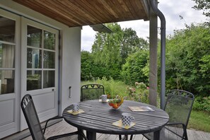 Une terrasse couverte avec une table dressée pour deux personnes, entourée de chaises, et offrant une vue sur un jardin luxuriant.