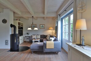 A cozy living room with a sofa, ottoman, and a fireplace. There are two pendant lights, a floor lamp, and a window with curtains.