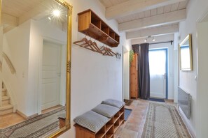 A hallway with a bench, a mirror, a coat rack, and a door leading to another room.