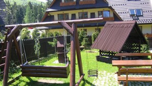 A wooden swing set, a picnic table, and a house with a balcony in a sunny outdoor setting. - 4-5 people, double room with kitchen u. balcony (Zakopane)