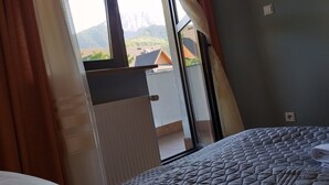 A bedroom with a bed, a window with curtains, and a view of buildings and mountains. - 4-5 people, double room with kitchen u. balcony (Zakopane)