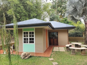 A small house with a sloped roof, a front door, and a patio area with outdoor seating. - Cottage (St Joseph)