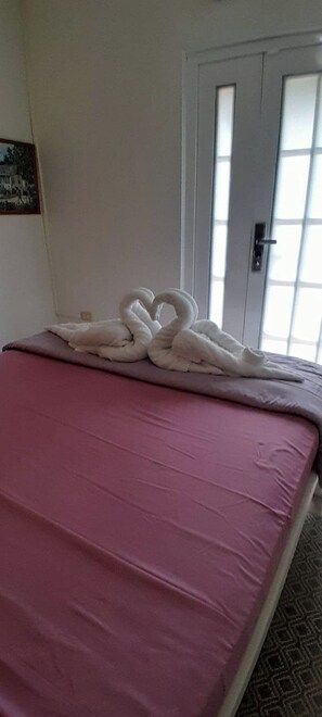 Habitación de hotel con una cama, una disposición de toallas con forma de corazón, una puerta y una ventana.