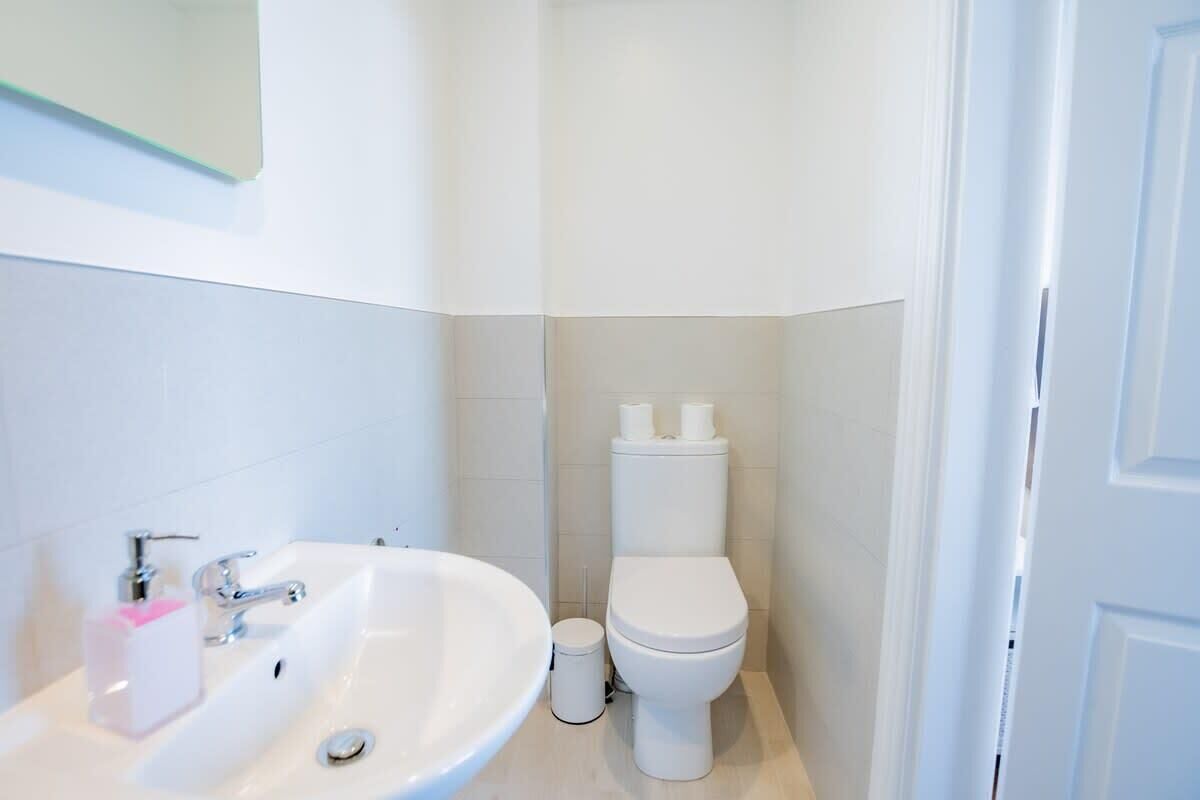 A bathroom with a white sink, toilet, and a trash bin.