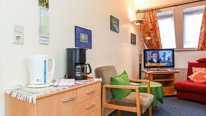 Huoneessa on puinen kaappi, vihreällä pöytäliinalla päällystetty pöytä, punainen sohva ja televisio, joka on sijoitettu jalustalle.