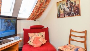 Huoneessa on punainen sohva, puinen tuoli, televisio ja seinälle ripustettu maalaus, jossa on kuvattuna hevosia.